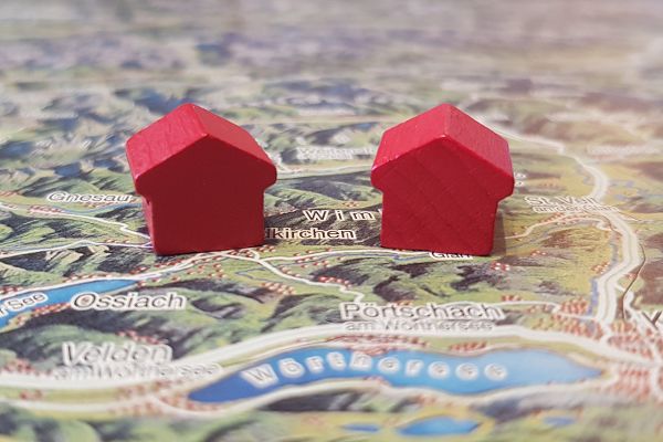 Symbolfoto mit zwei kleinen roten Spielzeug-Häusern, die auf einer Landkarte stehen.