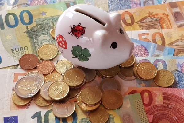 Ein Sparschwein steht auf nebeneinander und untereinander liegenden Geldscheinen und Münzen