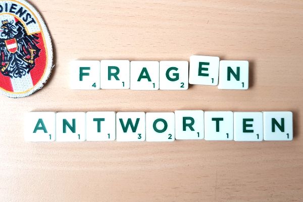Kleine Spielzeugplättchen mit den aufgedruckten Großbuchstaben „Fragen“ und „Antworten“, am linken oberen Bildschirmrand ist das Zivildienstabzeichen zu sehen.