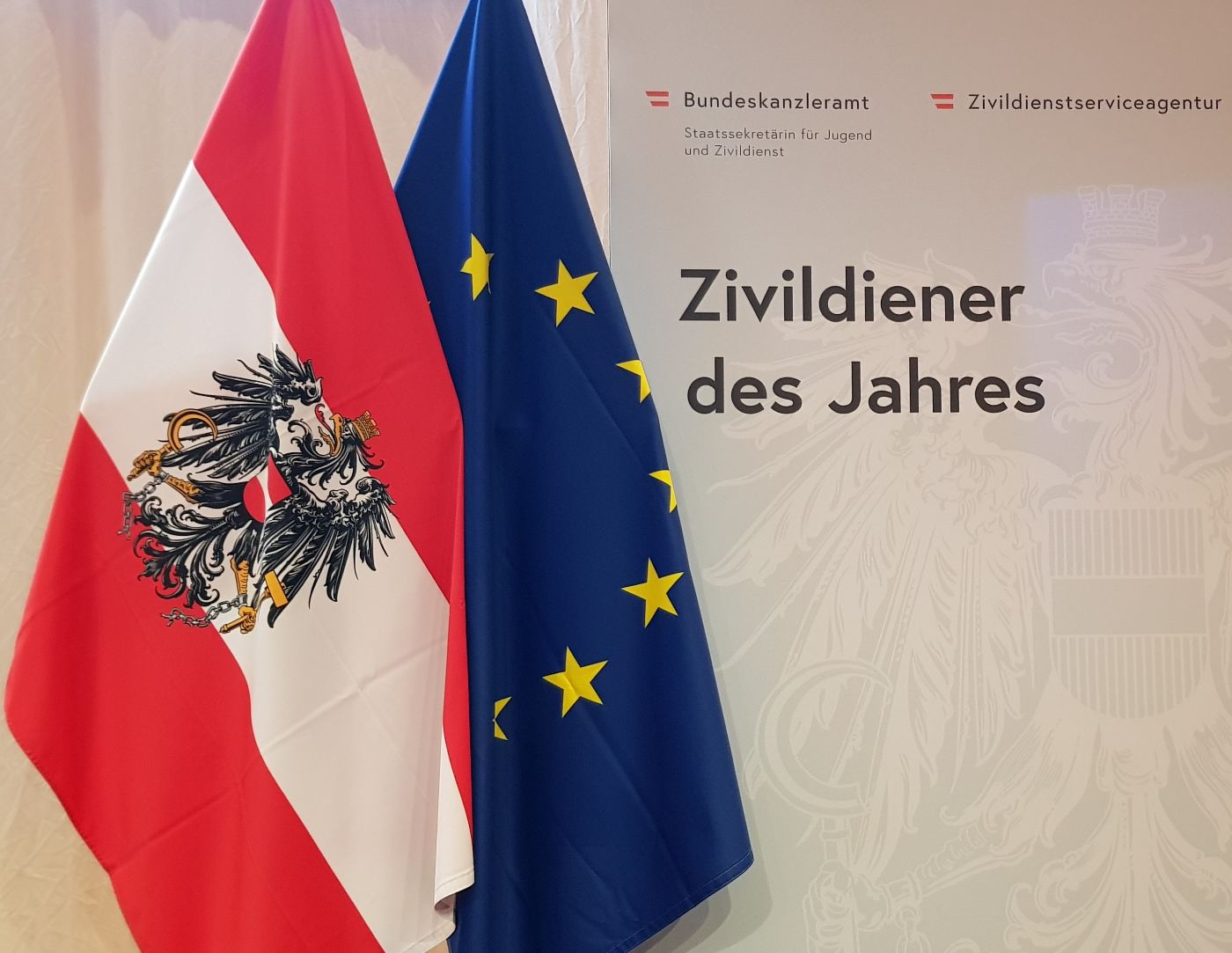 Eine Österreich-Fahne und eine EU-Fahne neben der Fotowand mit der Aufschrift "Zivildiener des Jahres"