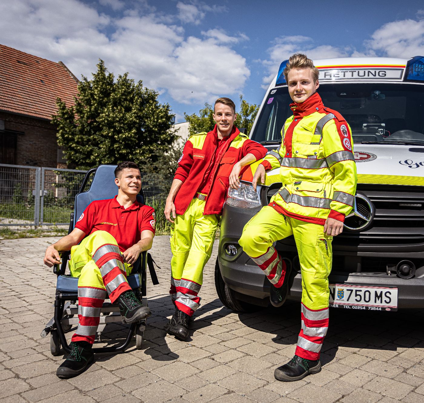 Drei Zivildiener in Uniform des Arbeiter-Samariter-Bundes Österreichs neben einem Rettungsauto