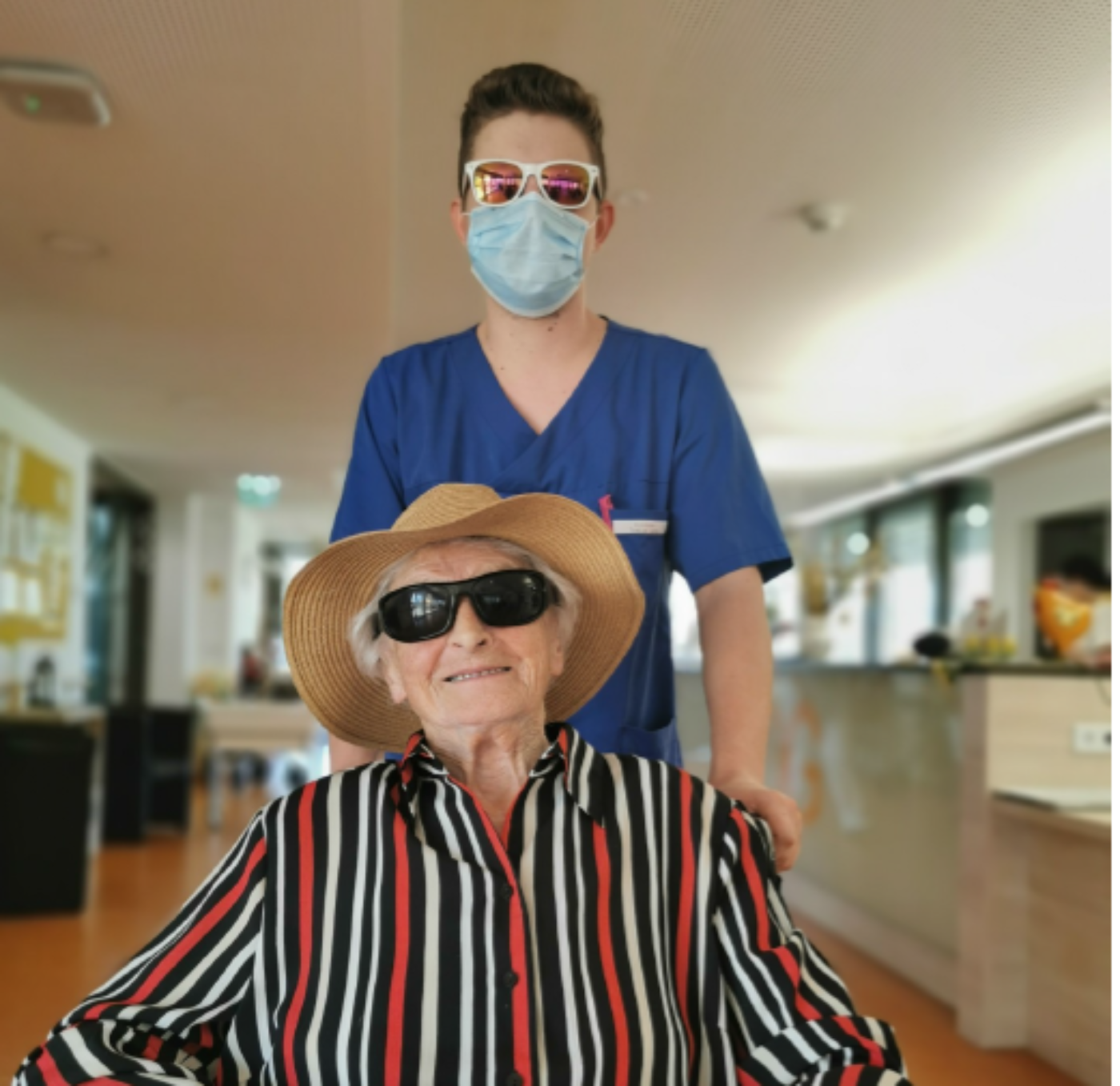 Ein Zivildiener im Bezirksseniorenzentrum Eggelsberg schiebt eine ältere Dame im Rollstuhl, beide tragen Sonnenbrillen