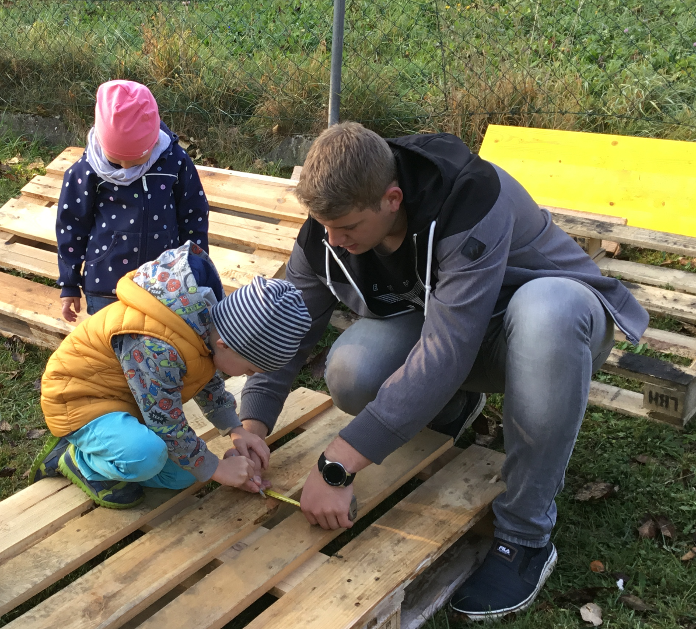 Ein Zivildiener und zwei Kinder im Kindergarten beim Basteln mit Holz im Freien