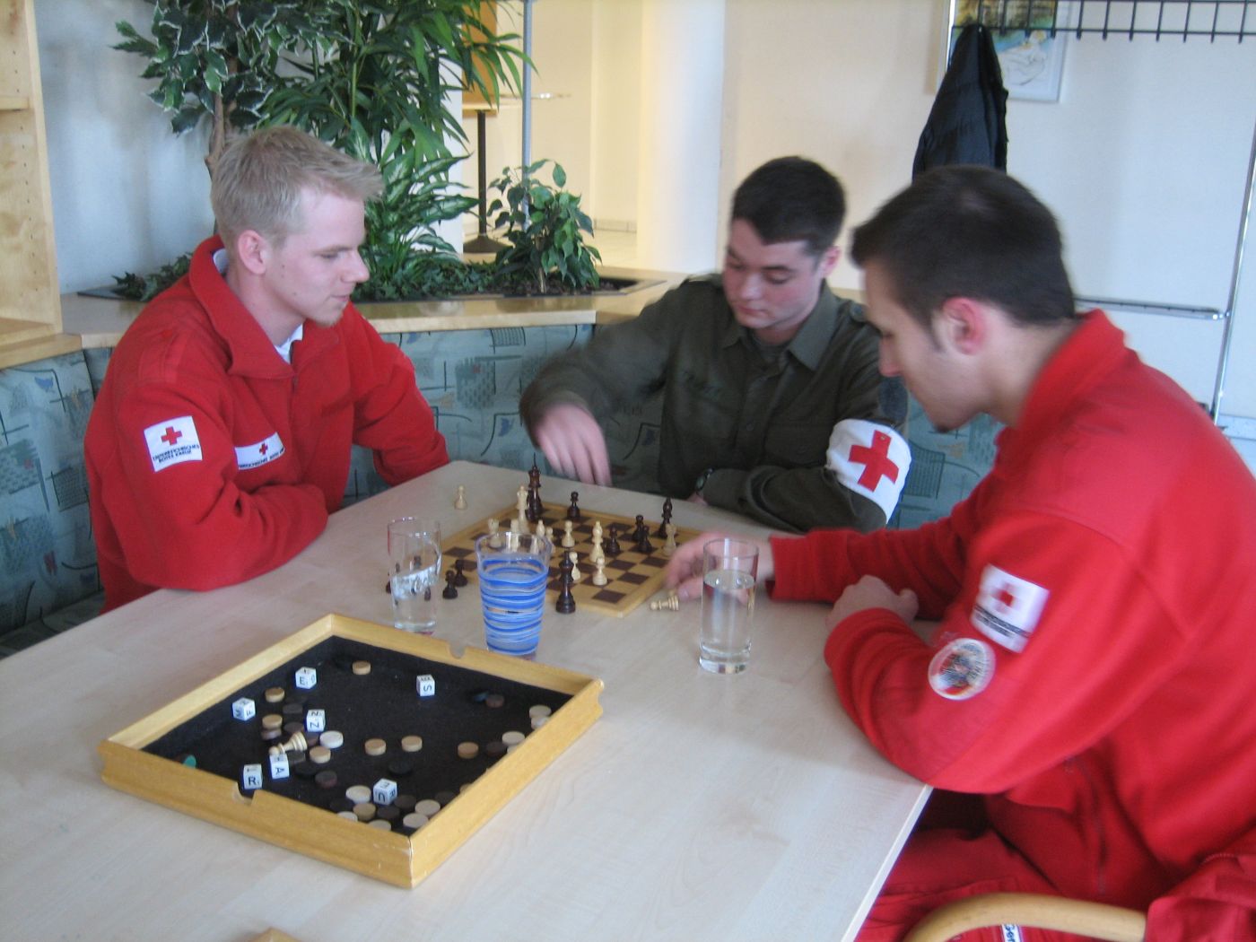 Zwei Zivildiener in Uniform des Österreichischen Roten Kreuzes und ein Grundwehrdiener in Uniform sitzen an einem Tisch und spielen Schach