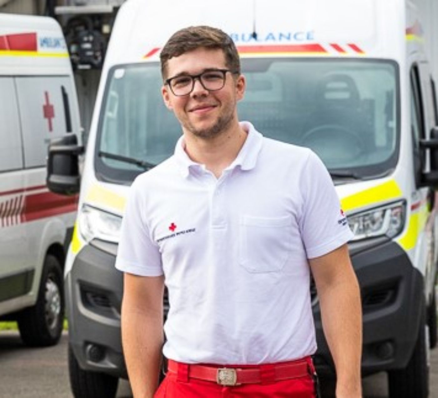 Ein Zivildiener in Uniform des Österreichischen Roten Kreuzes, im Hintergrund sind zwei Rettungsfahrzeuge zu sehen