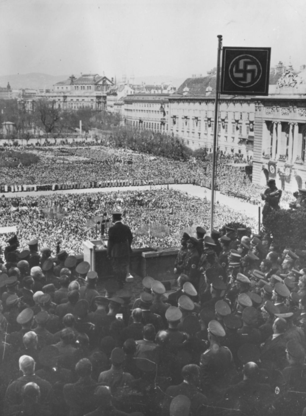 Schwarz-weiß-Foto zur Illustration. Das Foto zeigt Hitler am Balkon der Hofburg bei seiner historischen Rede. Er blickt auf die Menschenmenge auf dem Heldenplatz.