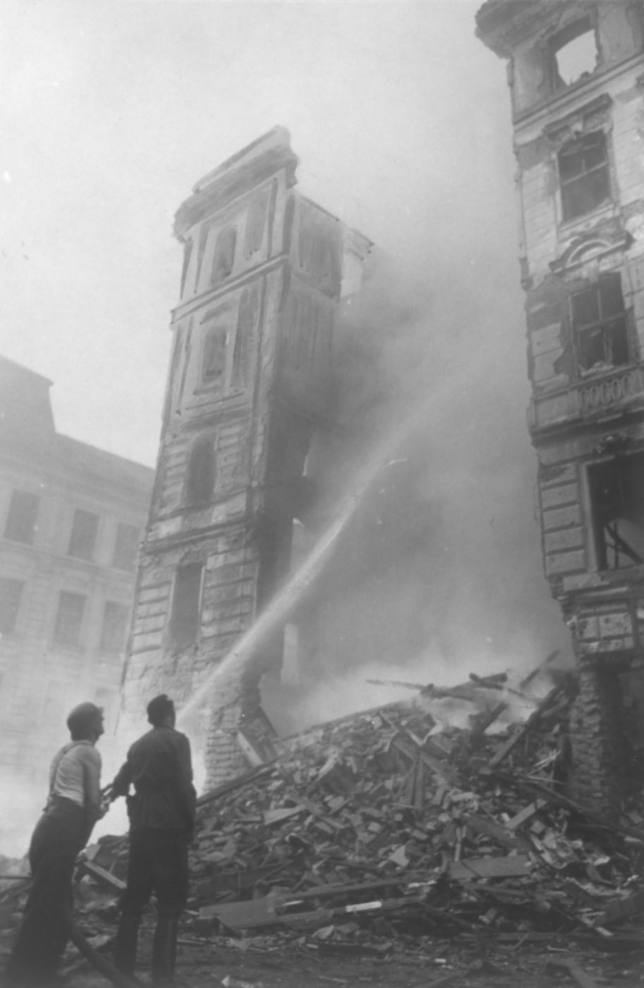 Schwarz-weiß-Bild zur Illustration. Das Bild zeigt zwei Männer bei Löscharbeiten an einem schwergetroffenen Wohnhaus, 8. Oktober 1944