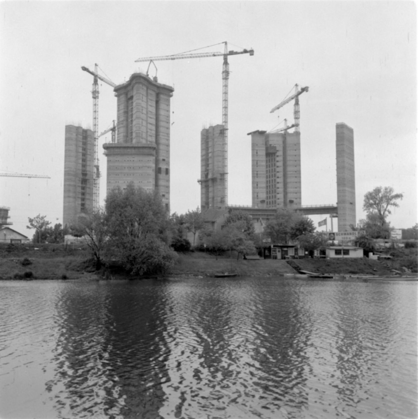 Schwarz-weiß-Foto zur Illustration. Das Bild zeigt mehrere Hochhäuser und Baukräne im Hintergrund. Im Vordergrund ist die Donau zu sehen.
