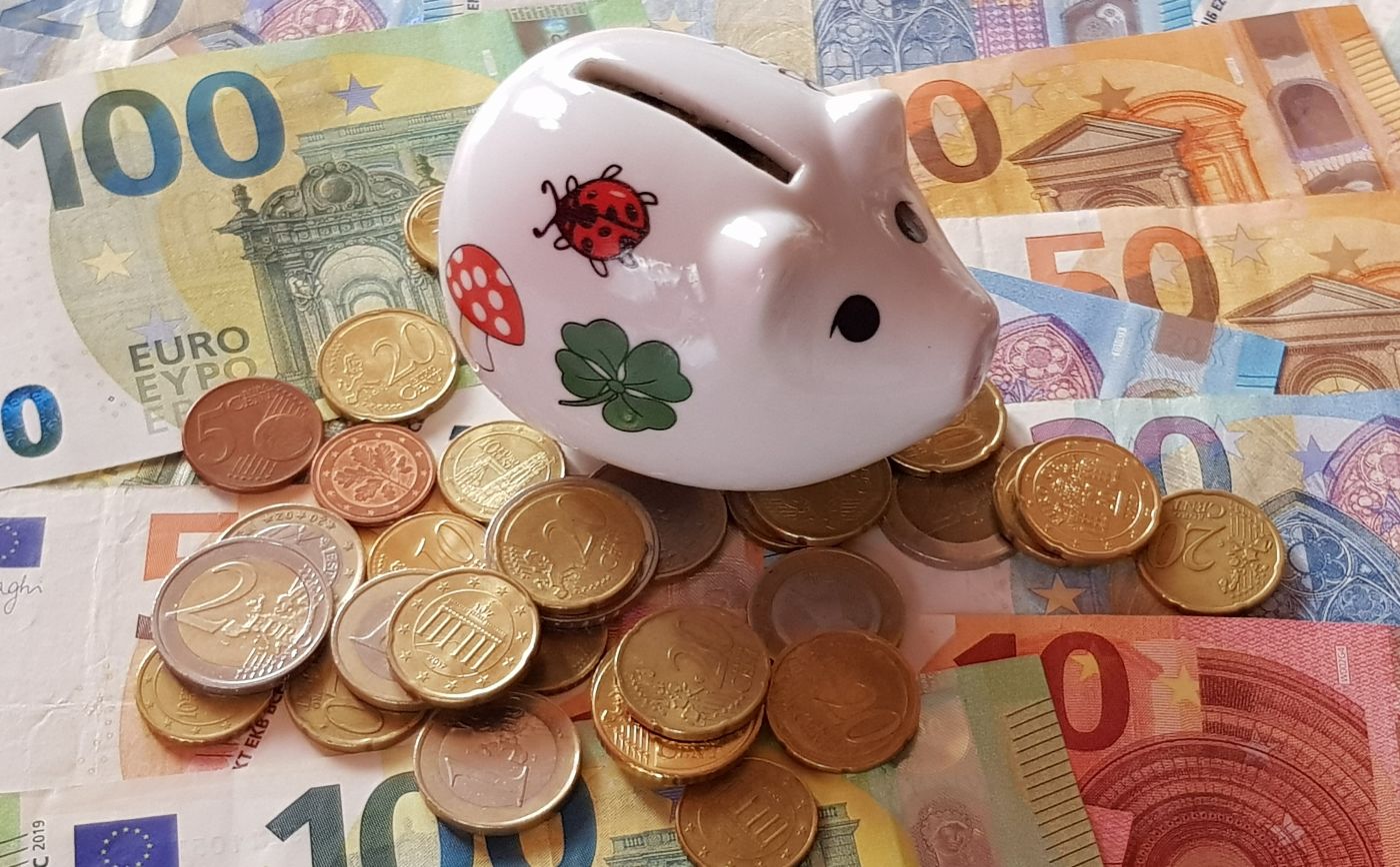 Ein Sparschwein steht auf nebeneinander und untereinander liegenden Geldscheinen und Münzen